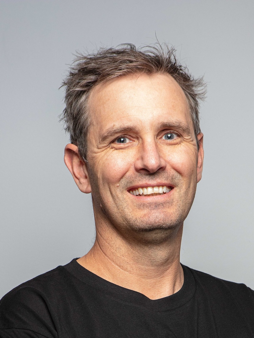 A headshot of a white man with browny grey hair, smiling