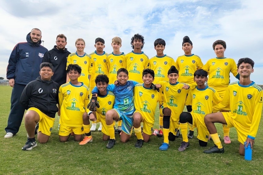 soccer players posing for photo with team coach wearing black jackets