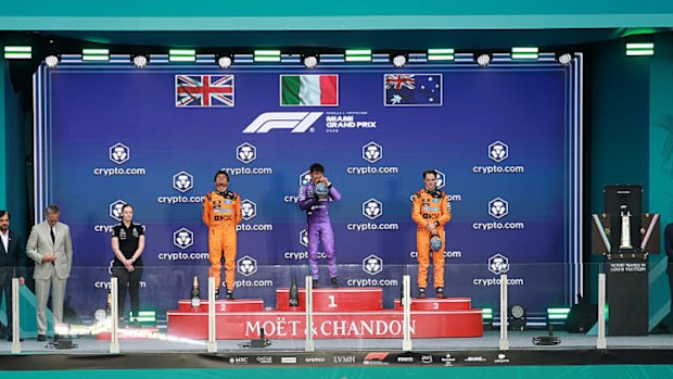 Three Formula 1 drivers stand on a podium.