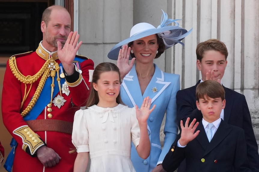 Prince William and Princess Kate and their three children, smile and wave on a balcony.