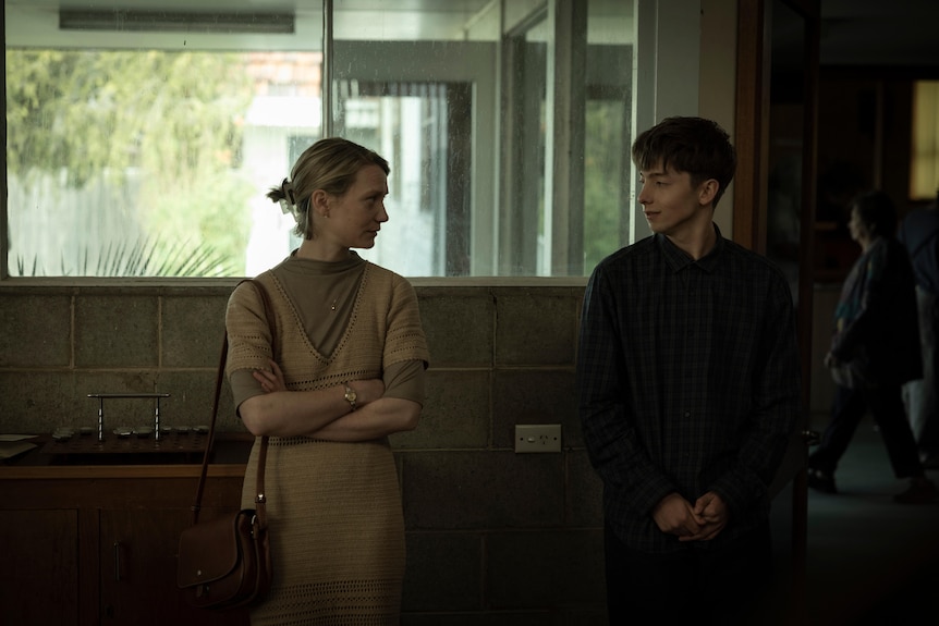 A young man and an adult woman stand two foot apart in a building