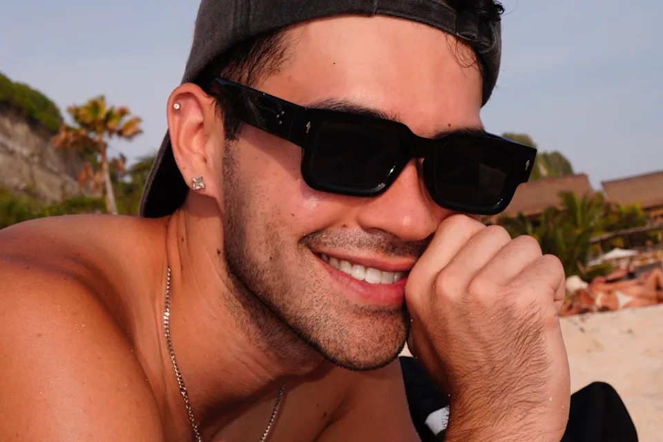 Jimmy laying on a beach smiling with sunglasses and hats.