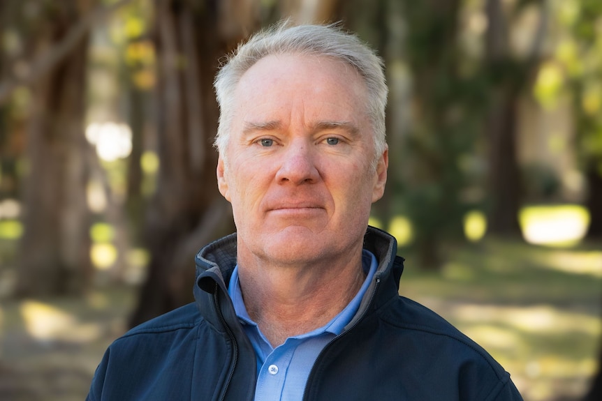Man with grey hair and blue eyes wears blue shirt and blue jacket