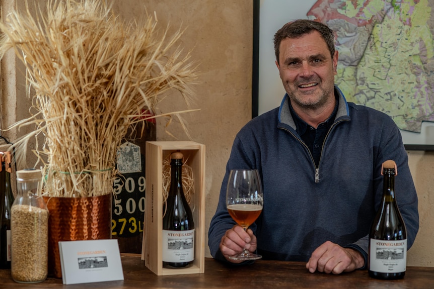 A man sitting surrounded by beers and holding a glass in his hand.