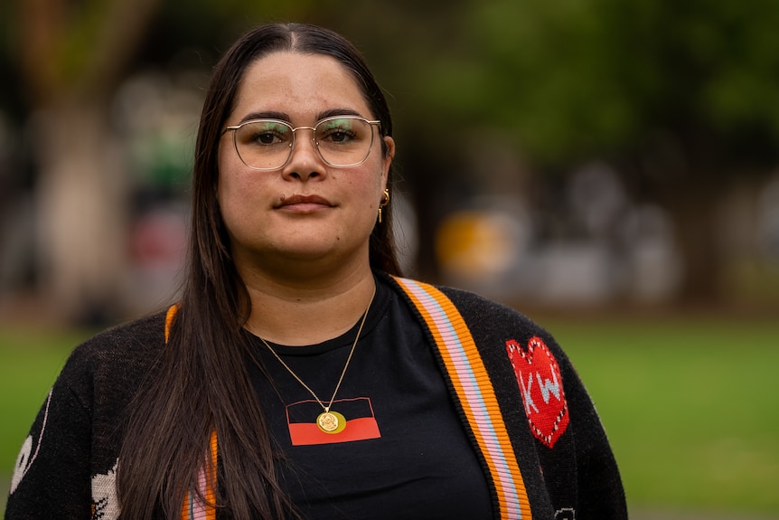 A woman wears glasses and a dark shirt with an Aboriginal flag.