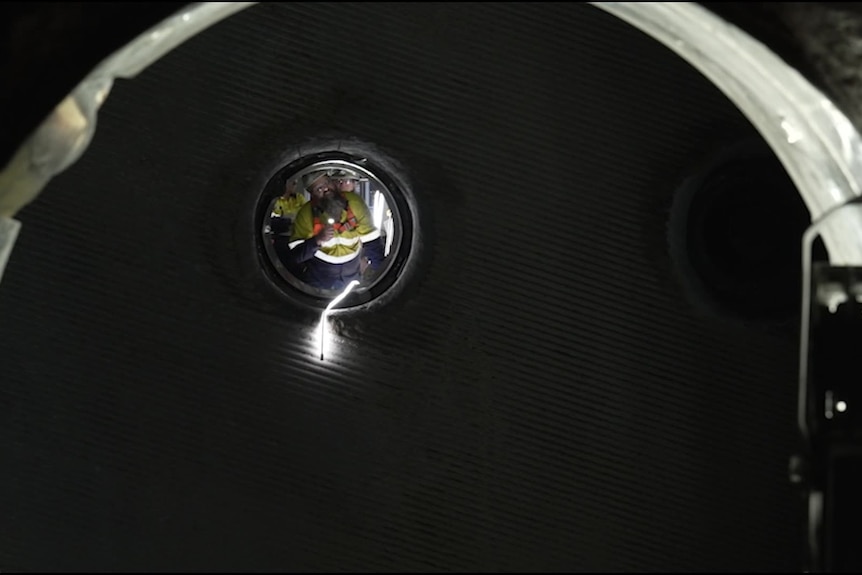 A worker in high vis shines a light into a dark tunnel while repairing a unit of a power station.