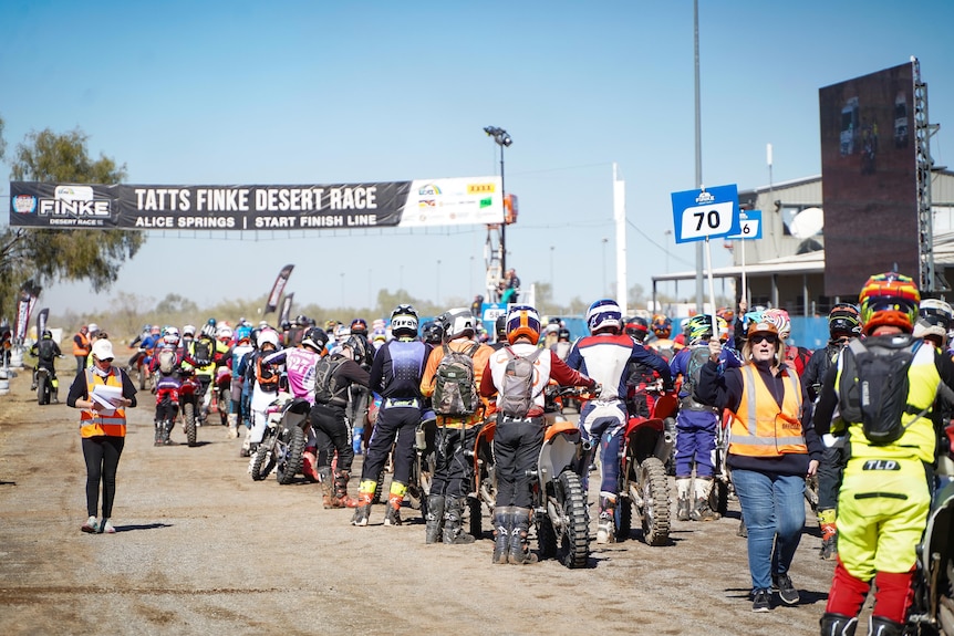 A large group of motorbike riders in a queue, each of them is wearing a helmet and standing alongside their bike.