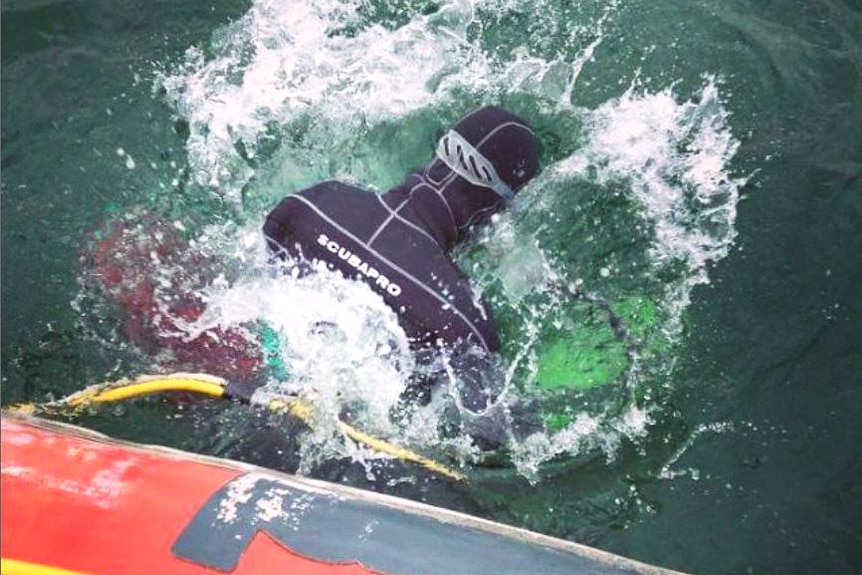 man in wetsuit dives into ocean