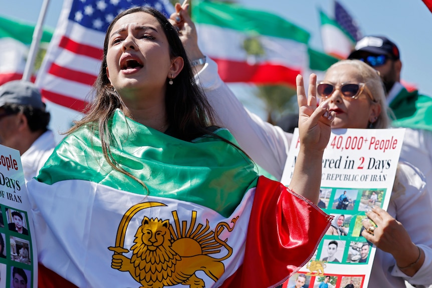 A woman draped in an Iranian 'Lion and Sun' flag yells at a protest