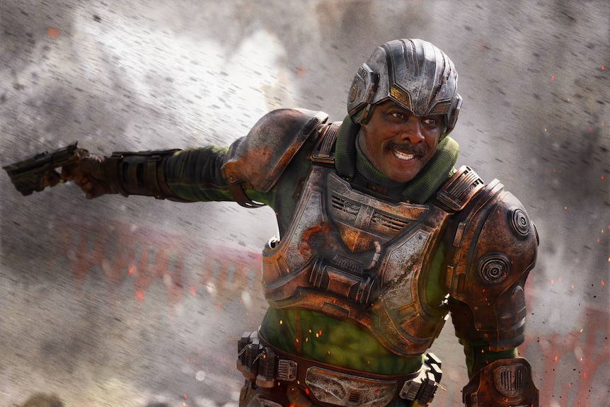 Idris Elba dressed in character as Man at Arms wearing a full body suit, moustache, in action scene.
