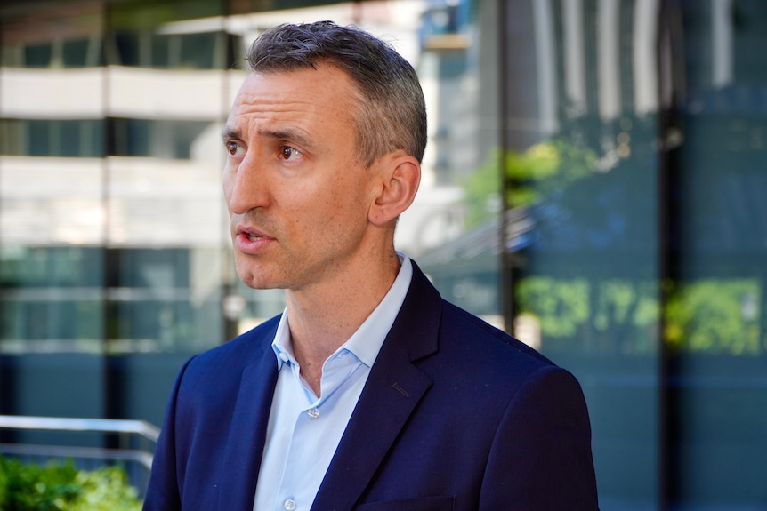 A man wearing a suit jacket and shirt speaks to reporters.