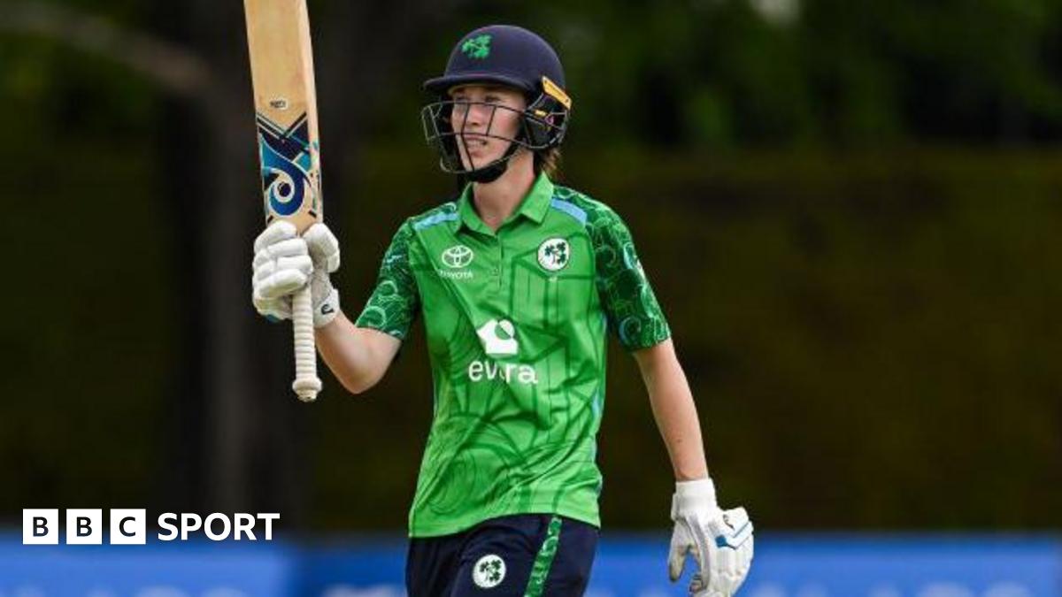 Orla Prendergast, in Ireland's largely green kit and wearing a blue batting helmet, raises her bat in acknowledgement of a half-century