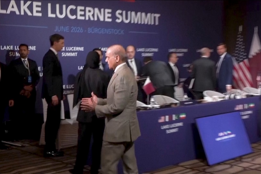 JD Vance stands near a sign watching as Iran's delegation walks out of the room.
