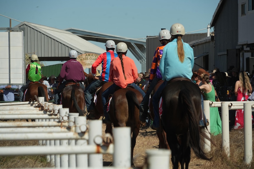 Horses parade past a crowd before an outback race 