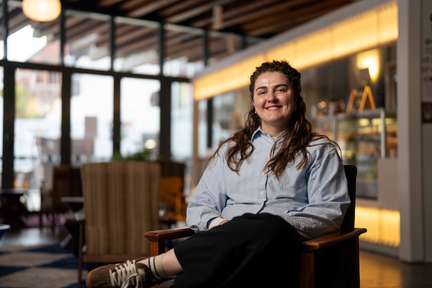 Woman sits on a chair in a cafe, smiling for photo