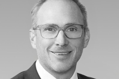 A man wearing glasses, smiles and looks at the camera