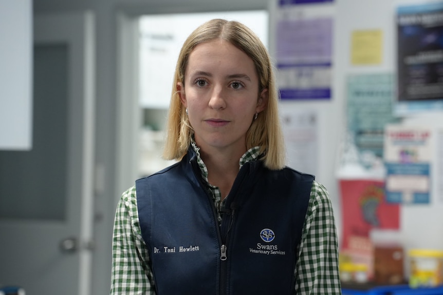 a woman in a collared shirt and vest standing in a vet practice