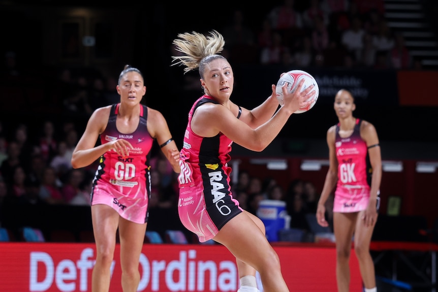 Three women playing netball in a stadium