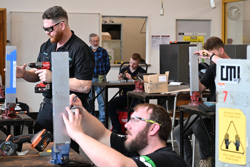 Four male locksmith apprentices use drills and tools in a workshop.