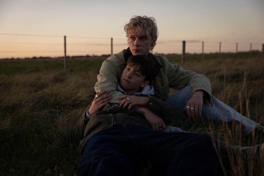 Two young men lie in a field together