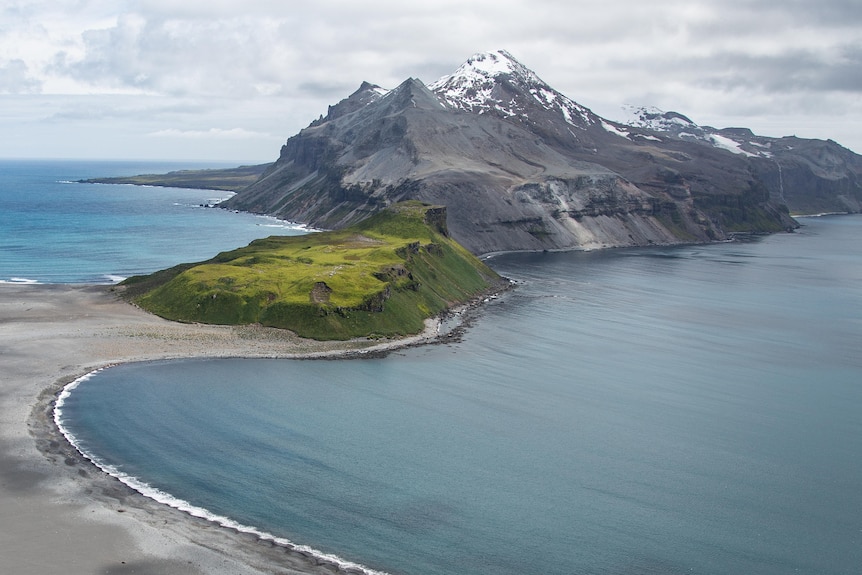 An aerial view of snow-covered Heard Island and McDonald Islands with beaches in the foreground.