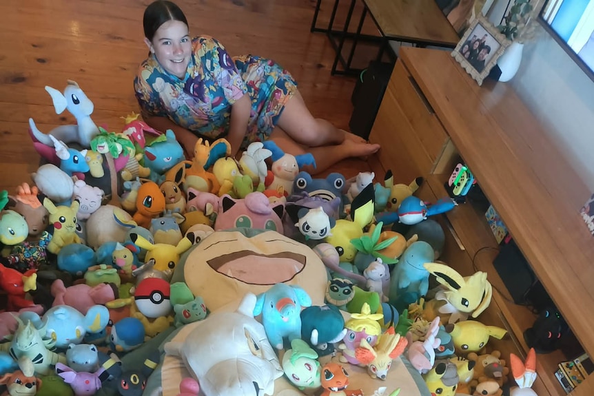 A young girl sits surrounded by more than 100 Pokemon plush toys.