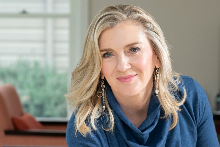 blonde woman in navy shirt with high collar smiling