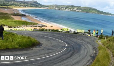 A corner of the track at the Donegal International Rally, overlooking a beach, with a handful of spectators standing behind the barrier