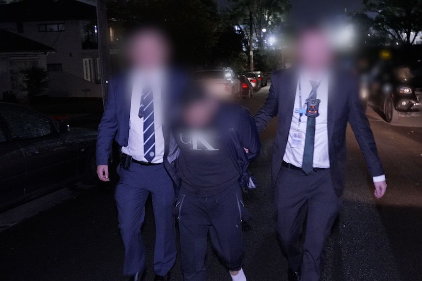 Man in black tracksuit, surrounded by police. Faces blurred