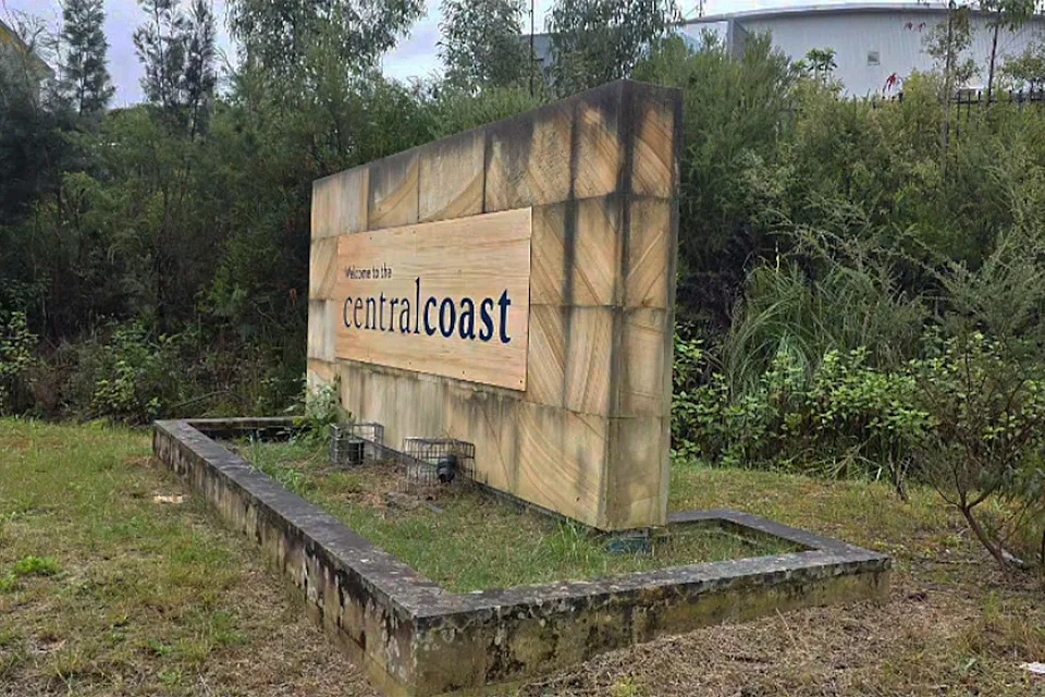 The Kariong sign before locals' efforts. Weeds, mould and unkempt grass is seen.