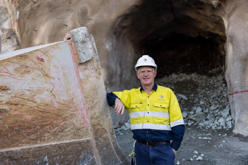 A miner in high-vis and hard hat next to the entrance to an underground access portal.