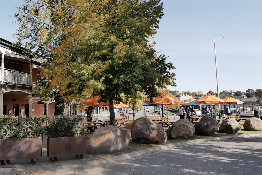 A pub with tables and umbrellas in the front, with a large tree creating shade.