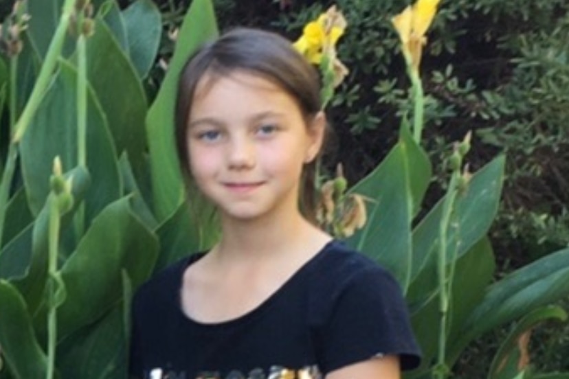 A smiling, dark-haired girl stands in a garden.