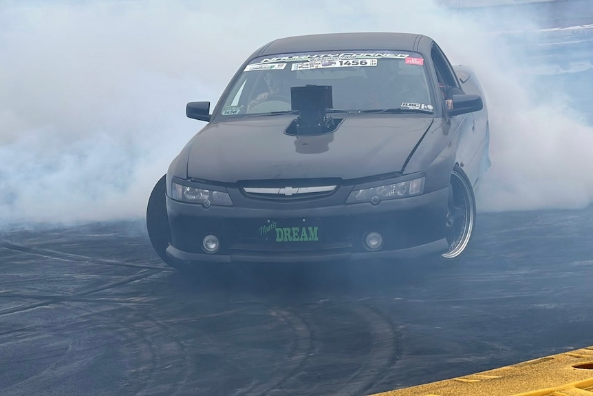 A woman drives a black ute as grey smoke appears at the back of the vehicle