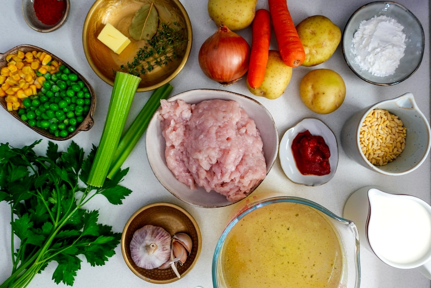 Chicken mince, stock, vegetables, parsley and cream sit on a bench along with several other ingredients.