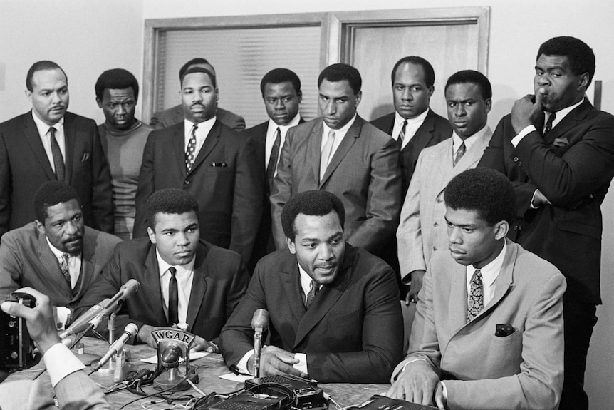 Muhammad Ali surrounded by athletes at a press conference.