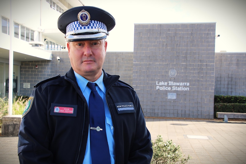 Male police offender standing in front of grey police station building