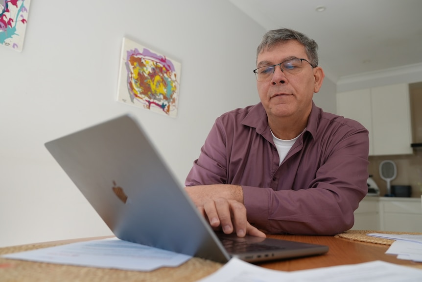 A man with a purple shirt and glasses reading over documents on his laptop