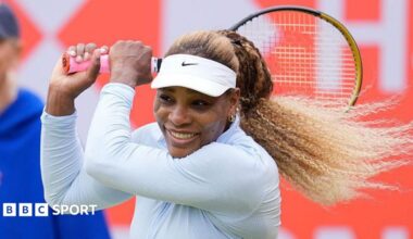Serena Williams, wearing white and smiling, plays a backhand