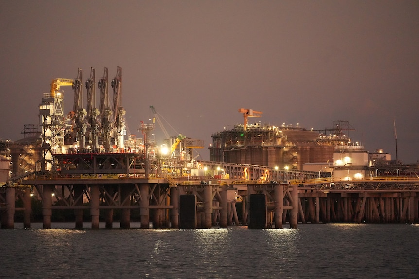 Evening / dusk shot of Darwin harbour, industrial site, with yellow lights glowing and cranes in view.