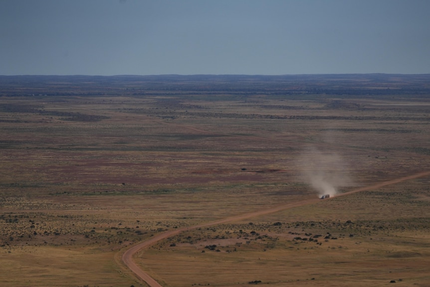 Taken from a plane, a wide flat landscape with a dirt road through the middle, and a truck driving along