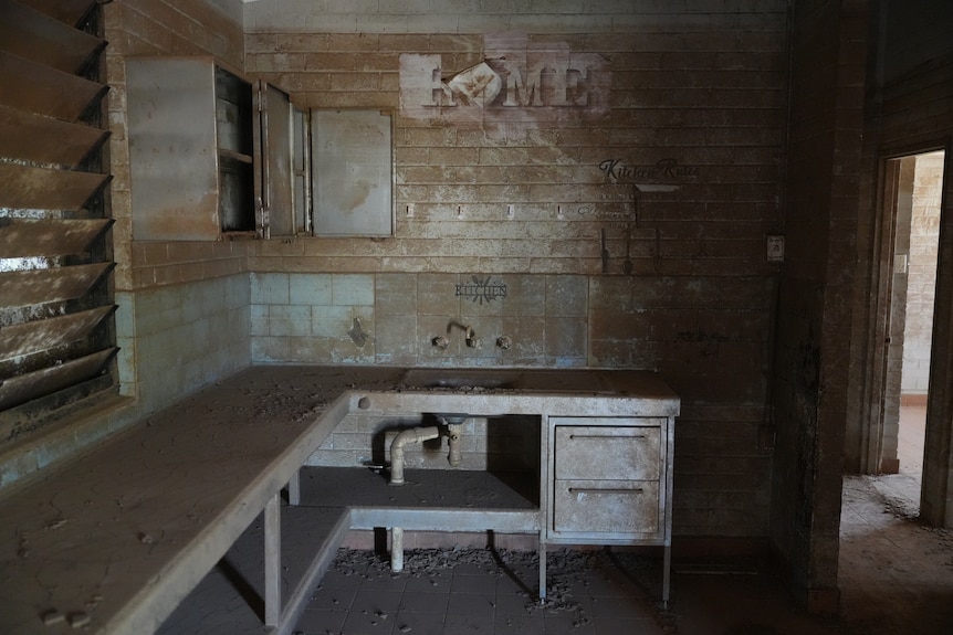 A basic kitchen bench and sink inside a home is coated in mud
