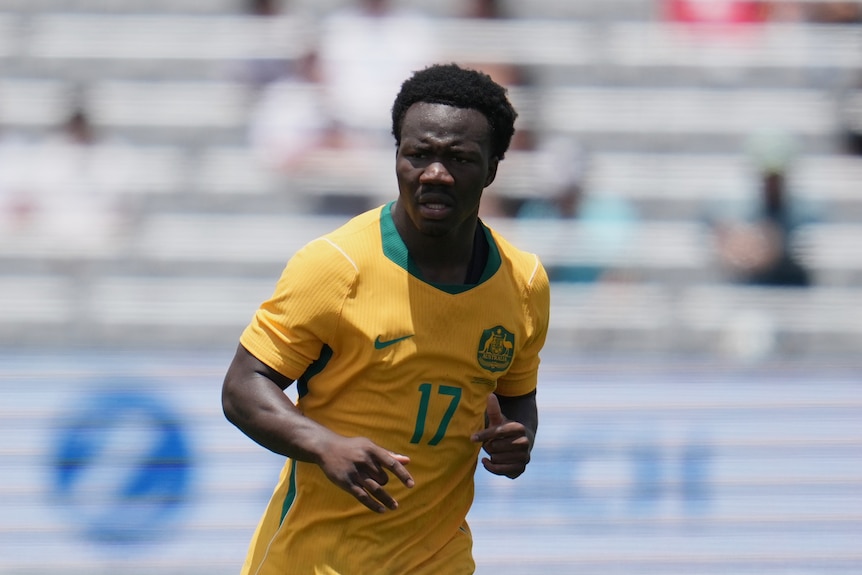 A man in a yellow jersey runs on a soccer pitch.