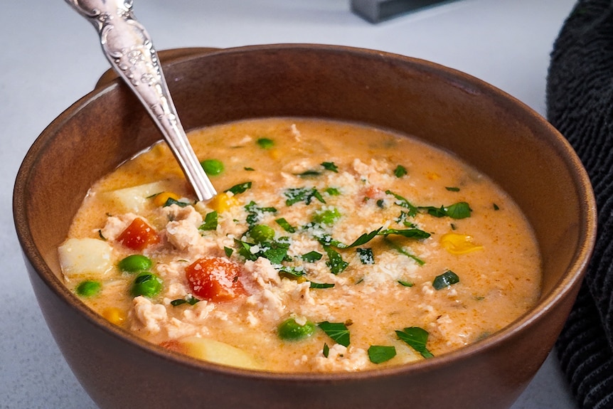 A small bowl of soup, with a spoon in it, sits on a bench.
