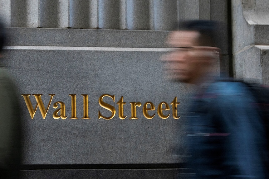 A person walks past a building with "Wall Street" lettered in gold on it.