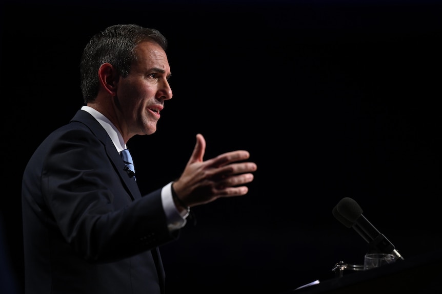 Side view of Jim Chalmers speaking at a lecturn, hands raised