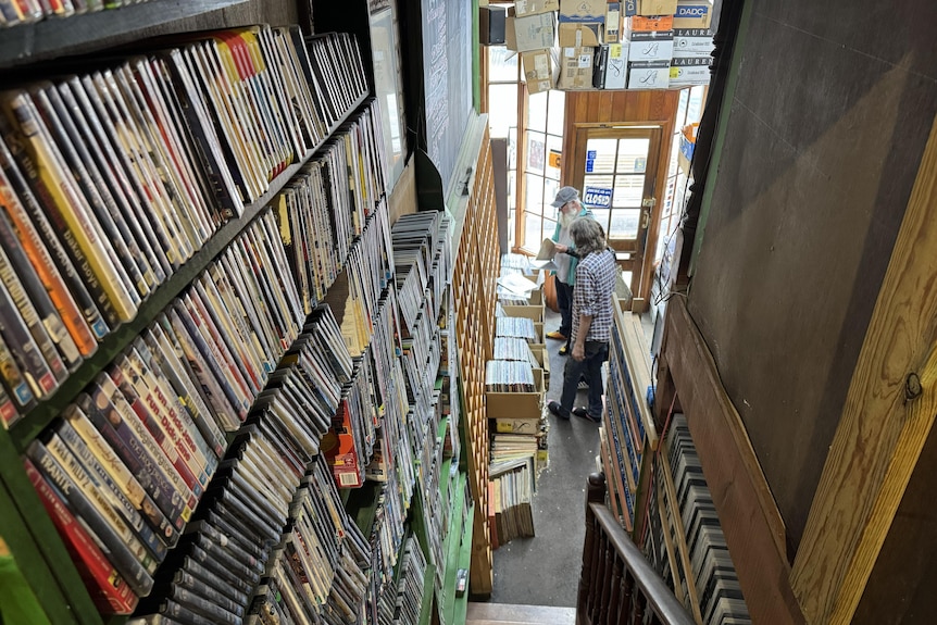 Shelves of videos and DVDs along a staircase with two men looking at video cases