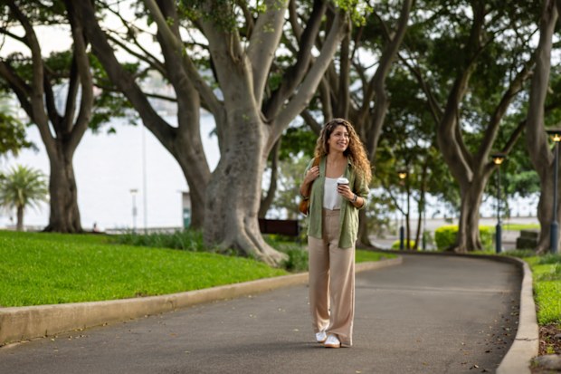 Happy young woman walking around the Royal Botanic Gardens in Sydney while drinking coffee and smiling