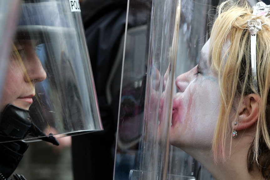 A person in clown makeup kisses a police guard