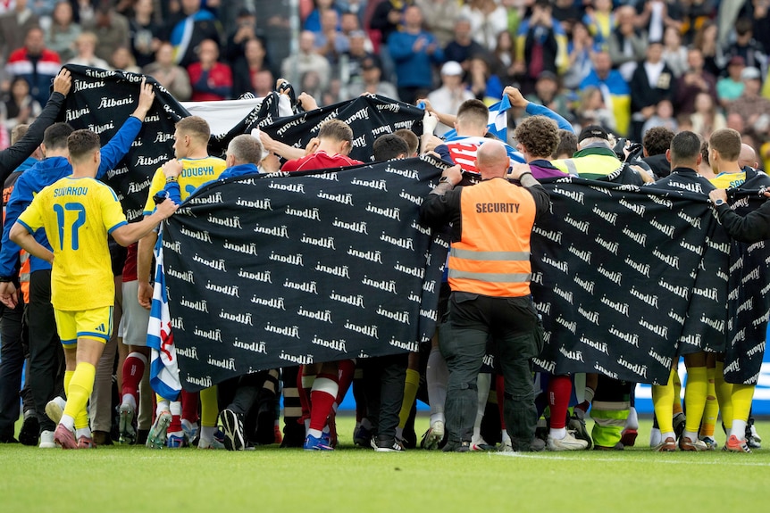 Denmark's and Ukraine's players accompany Christian Eriksen to a waiting ambulance.